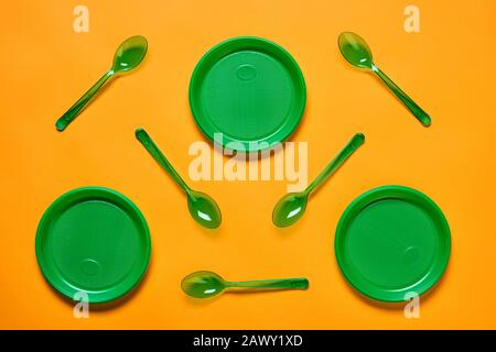Horizontal flat lay conceptual shot of green plastic spoons and plates on bright orange background Stock Photo