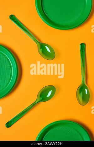 Vertical flat lay conceptual pattern shot of green plastic spoons and plates on bright orange background Stock Photo