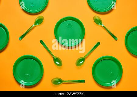 Horizontal flat lay conceptual shot of pattern made of green plastic plates and spoons on bright orange background Stock Photo