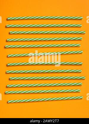Green and white striped plastic drinking straws on bright orange background, vertical flat lay shot Stock Photo