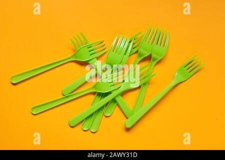 Disposable light green plastic forks lying on bright orange background, horizontal conceptual flat lay shot Stock Photo