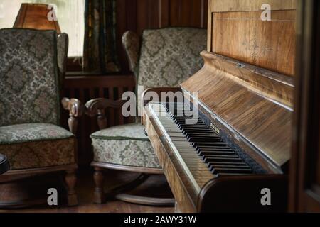 Vintage room with a luxurious piano on a rustic and wooden floor and two old armchairs in front of a dirty window Stock Photo