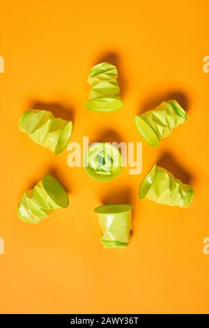 Vertical flat lay pattern shot of used light green plastic cups on bright orange background Stock Photo