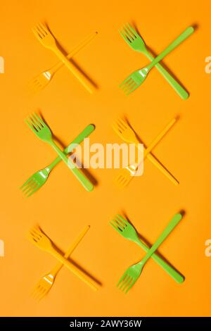 Vertical conceptual flat lay shot of X marks made of disposable light green and orange plastic forks on orange background Stock Photo