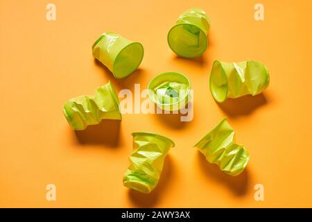 Used disposable light green plastuc cups lying on bright orange surface, horizontal high angle shot Stock Photo
