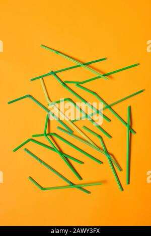 Vertical conceptual flat lay shot of disposable plastic drinking straws lying on orange surface Stock Photo