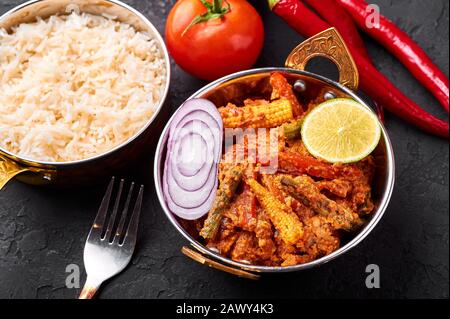 Vegetable Jalfrezi in copper kadai with basmati rice at black slate background. Jalfrezi is Indian Cuisine dish with stir fried vegetables and tomato- Stock Photo