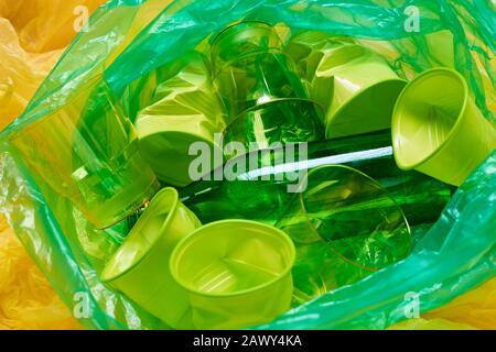 Horizontal from above shot of green plastic bin bag full of green plastic litter on yellow plastic background Stock Photo