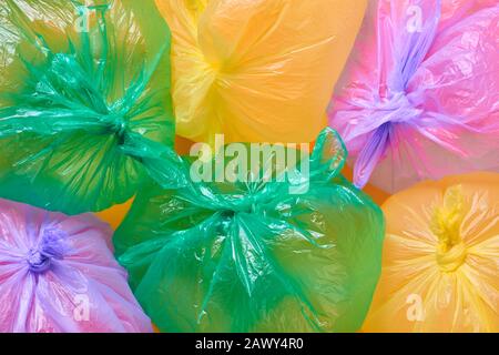 Green, yellow and violet plastic garbage bags full of air on orange background, horizontal flat lay conceptual shot Stock Photo