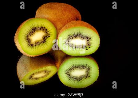 Kiwi fruit cut in half and sitting on a mirrored surface with reflections and a black background Stock Photo