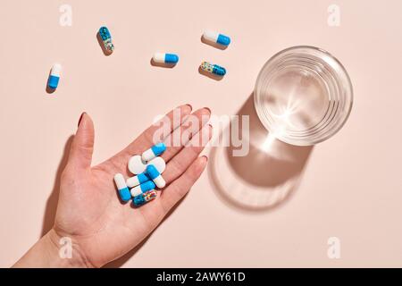 Various medicaments in women's hand with glass of water on pale pink background, horizontal flat lay shot Stock Photo