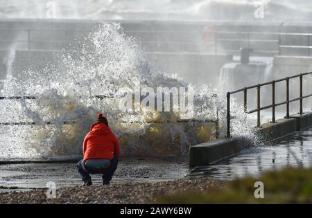 Shoreham UK 10th February 2020 - A walker watches the waves crash in at the entrance of Shoreham harbour in Sussex as the tail end of Storm Ciara gradually blows through Britain after battering most of the country over the weekend : Credit Simon Dack / Alamy Live News Stock Photo