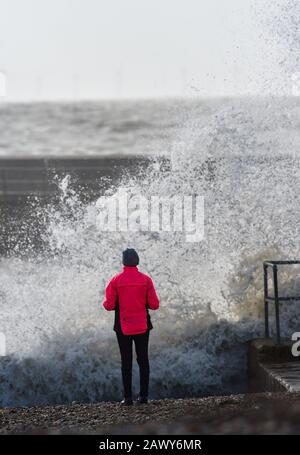 Shoreham UK 10th February 2020 - A walker watches the waves crash in at the entrance of Shoreham harbour in Sussex as the tail end of Storm Ciara gradually blows through Britain after battering most of the country over the weekend : Credit Simon Dack / Alamy Live News Stock Photo