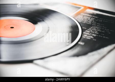 A black retro vinyl record with music recorded on it lies on the paper cover of the music album. Stock Photo