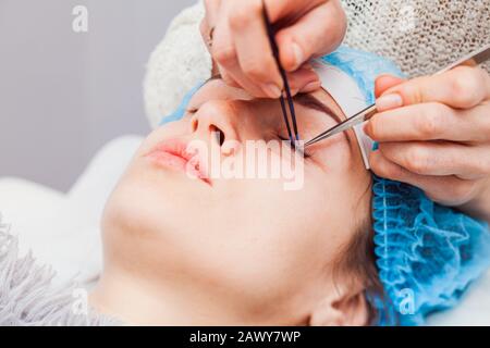 Stylist holding tweezers, tongs and making lengthening lashes for girl in a beauty salon Stock Photo