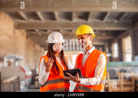 Smiling students doing practical work at factory. Professional people with helmets using tablet Stock Photo
