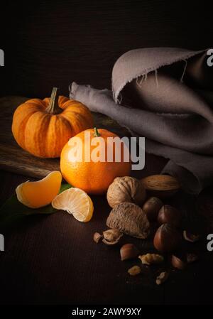 Autumn still life with mixed nuts , mini pumpkin and orange Stock Photo