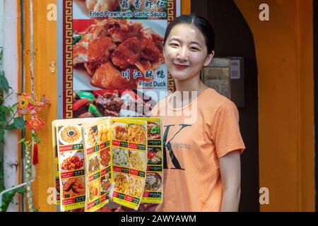 Young woman working as a waitress displaying a menu from the restaurant she works in, Chinatown, Singapore, Asia Stock Photo