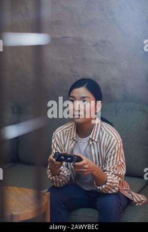 Vertical portrait of young Asian woman playing videogames via gaming console Stock Photo