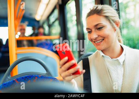 Smiling young woman using smart phone on bus Stock Photo