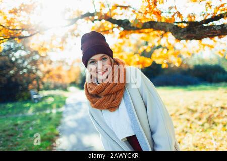Portrait happy young woman in stocking cap and scarf in sunny autumn park Stock Photo