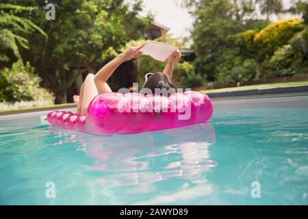 Woman reading book on inflatable raft in sunny summer swimming pool Stock Photo