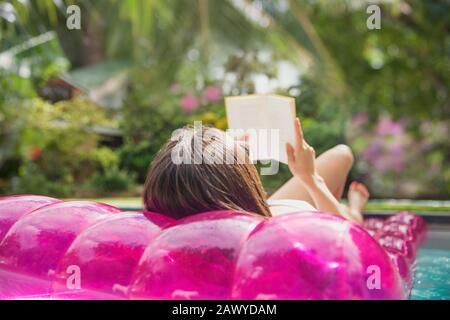 Woman relaxing, reading book on inflatable raft in swimming pool Stock Photo