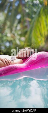 Serene woman relaxing, sleeping on inflatable raft in sunny swimming pool Stock Photo