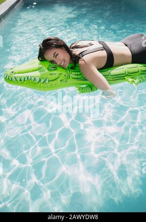 Portrait carefree woman floating on inflatable alligator raft in sunny summer swimming pool Stock Photo
