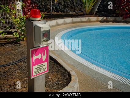 Swimming pool emergency stop button, with blue pool next to it. Stock Photo