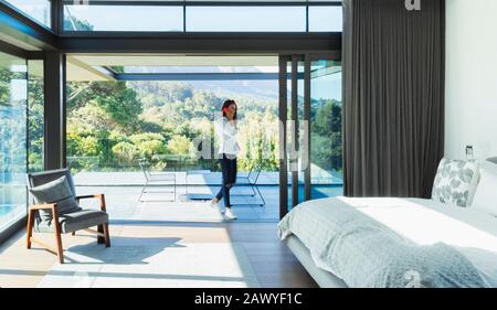 Woman talking on smart phone in patio doorway of modern, luxury bedroom Stock Photo