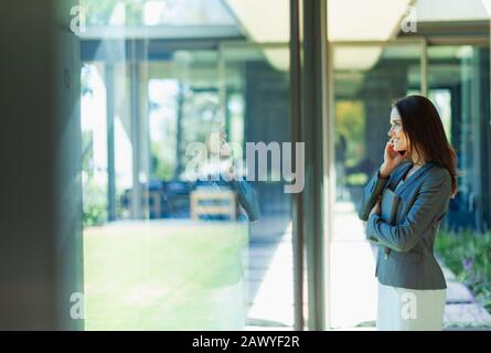 Businesswoman talking on smart phone at window Stock Photo