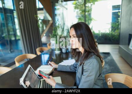 Businesswoman working from home, using smart phone and laptop Stock Photo