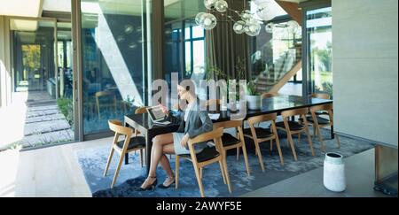 Businesswoman working from home, using smart phone at modern dining table Stock Photo