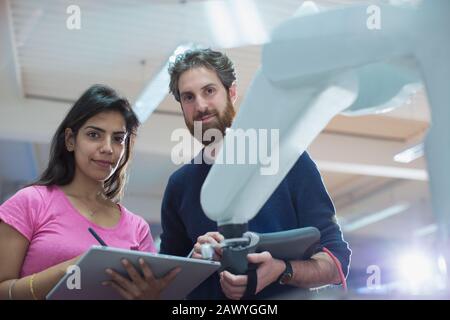 Portrait confident engineers with digital tablet programming robotic arm in office Stock Photo