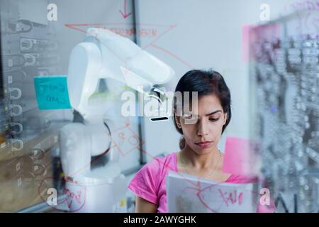 Female engineer with paperwork planning, programming robotic arm Stock Photo