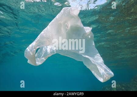 Plastic pollution underwater in ocean, a white plastic bag drifts below water surface Stock Photo