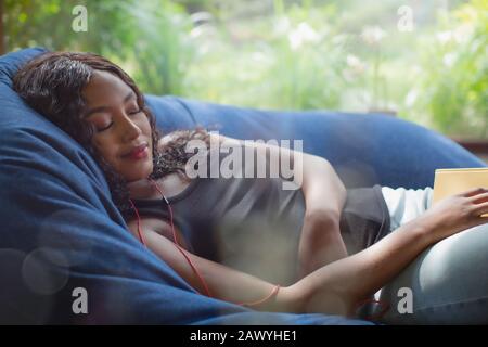 Serene young woman with headphones listening to music in beanbag chair Stock Photo