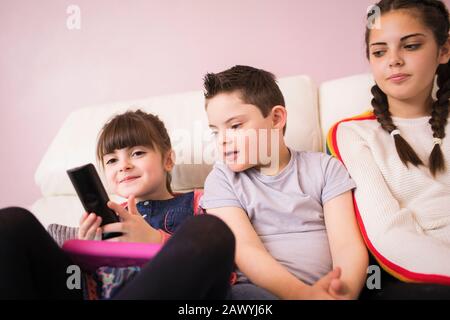 Sisters and brother with Down Syndrome watching TV on sofa Stock Photo