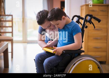 Boy with Down Syndrome using digital tablet in wheelchair Stock Photo