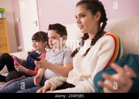 Boy with Down Syndrome watching TV with siblings on sofa Stock Photo