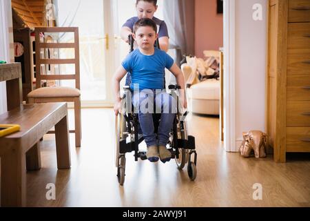 Boy pushing brother with Down Syndrome in wheelchair Stock Photo