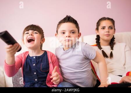 Sisters and brother with Down Syndrome watching TV on sofa Stock Photo