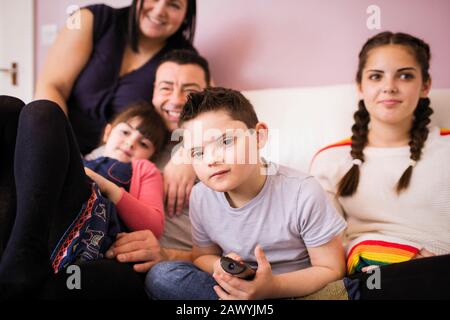 Portrait boy with Down Syndrome watching TV with family on sofa Stock Photo