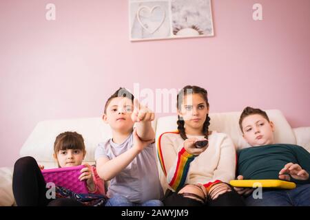 Down Syndrome boy watching TV with siblings on sofa Stock Photo