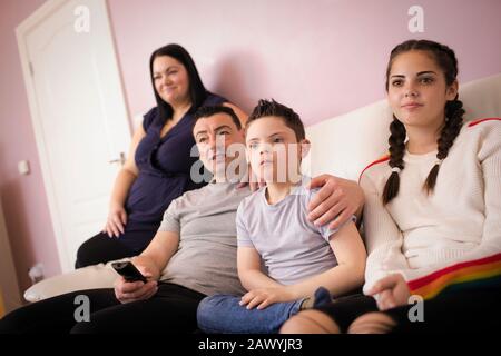 Family with Down Syndrome son watching TV on living room sofa Stock Photo