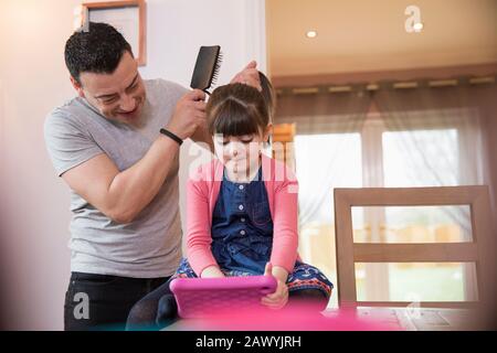 Father brushing hair of daughter using digital tablet Stock Photo