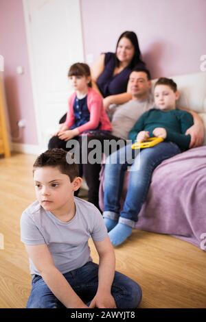 Boy with Down Syndrome watching TV with family in living room Stock Photo