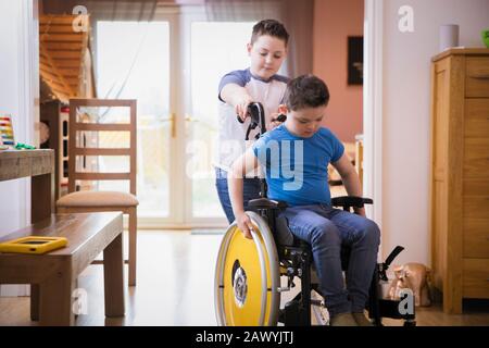 Boy pushing brother with Down Syndrome in wheelchair Stock Photo