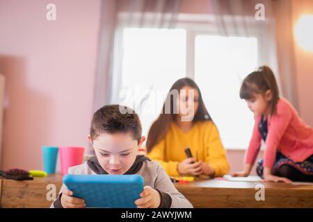 Boy with Down Syndrome using digital tablet at dining room table Stock Photo